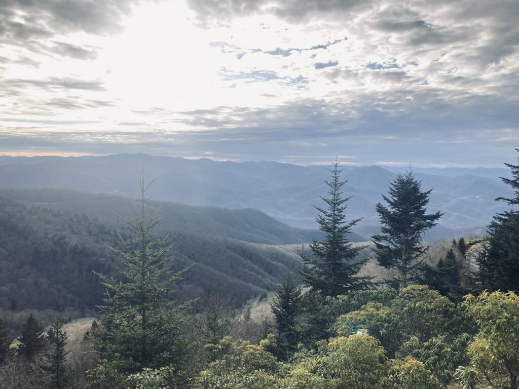 Sunlight breaking over misty forested mountains from an overlook on one of Adam Neuerburg’s hikes