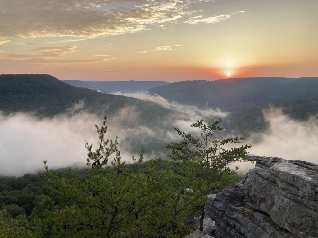 The sun rising over fog-filled valleys from a rocky overlook on a hike by Adam Neuerburg