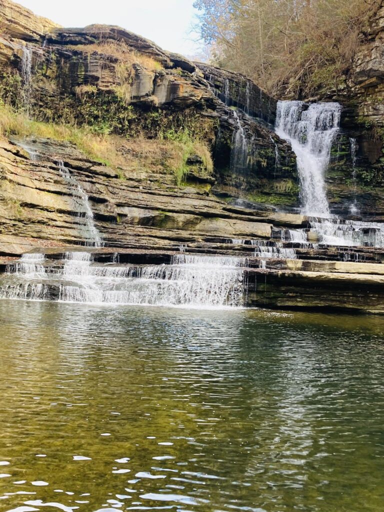 A tiered waterfall spilling over layered rock into a calm pool, found by Adam Neuerburg on a hike