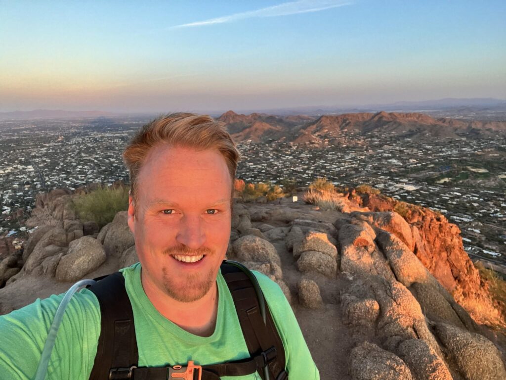 Adam Neuerburg hiking to a summit above a city at golden hour
