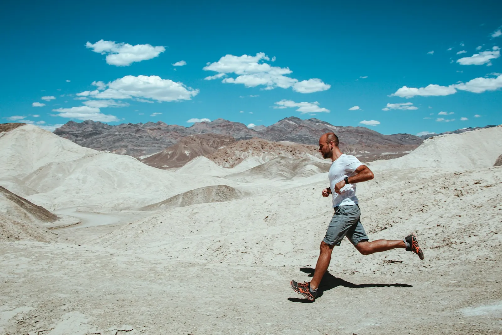 Runner on a pale desert trail with mountains and blue sky behind