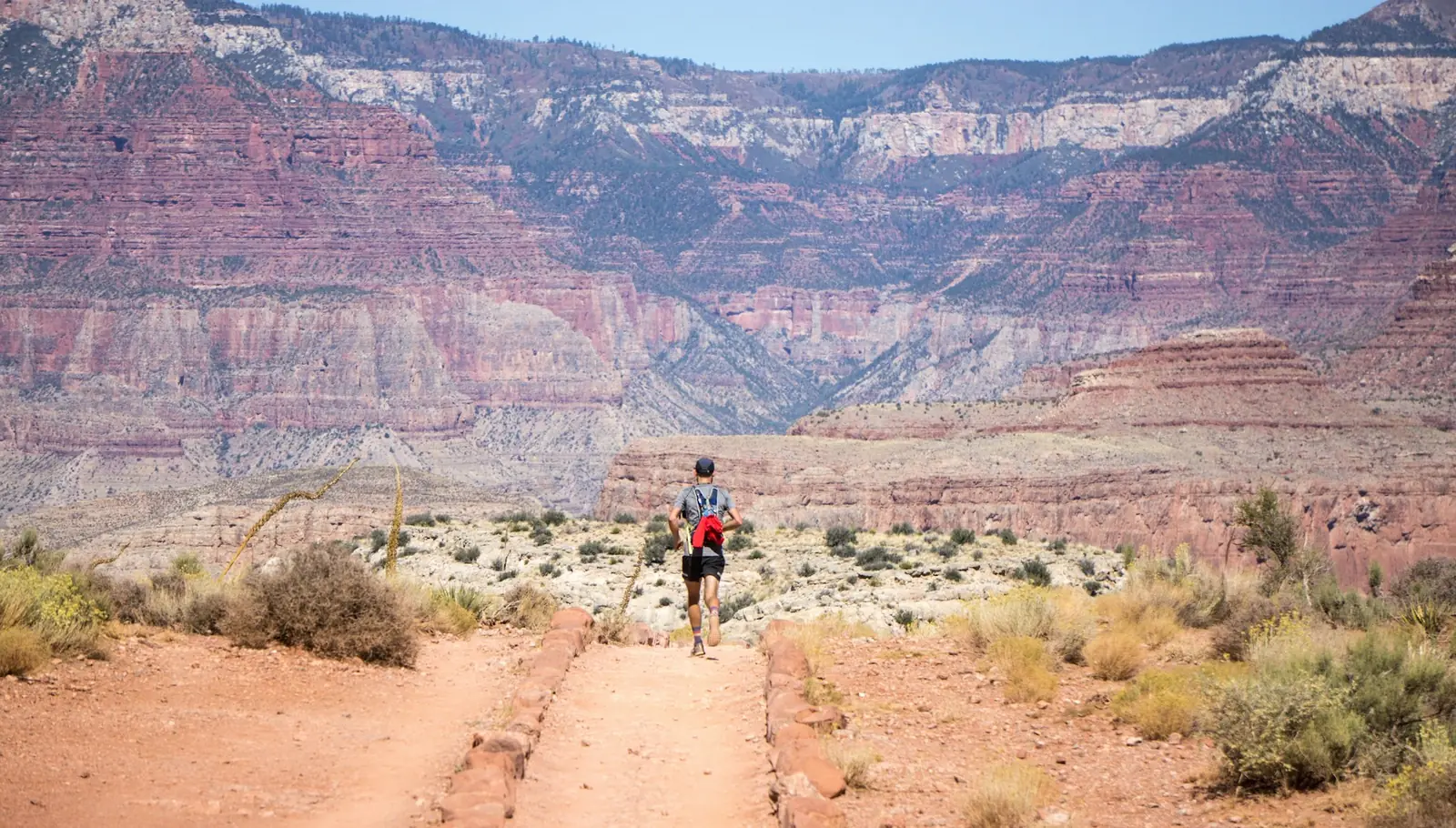 Hiker on a red desert trail with canyon walls in the distance