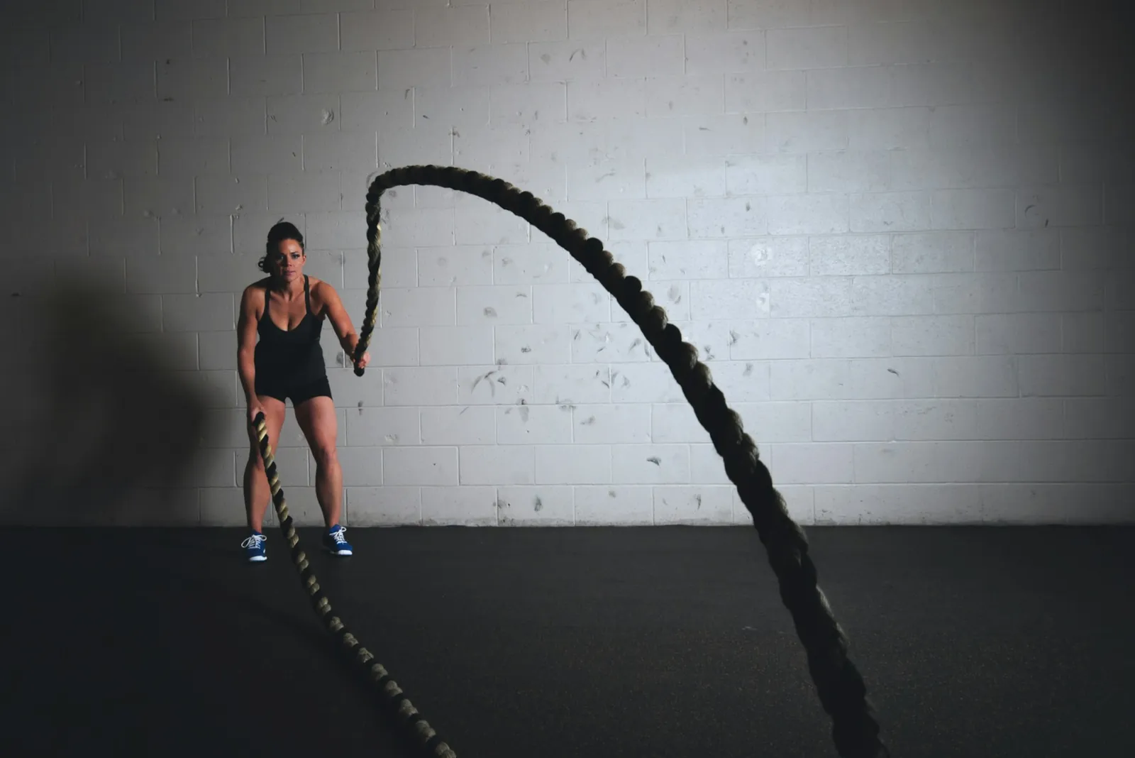 Athlete working battle ropes against a white brick wall