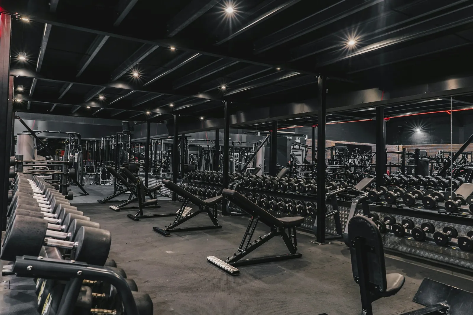 Rows of dumbbells and benches in a dimly lit gym