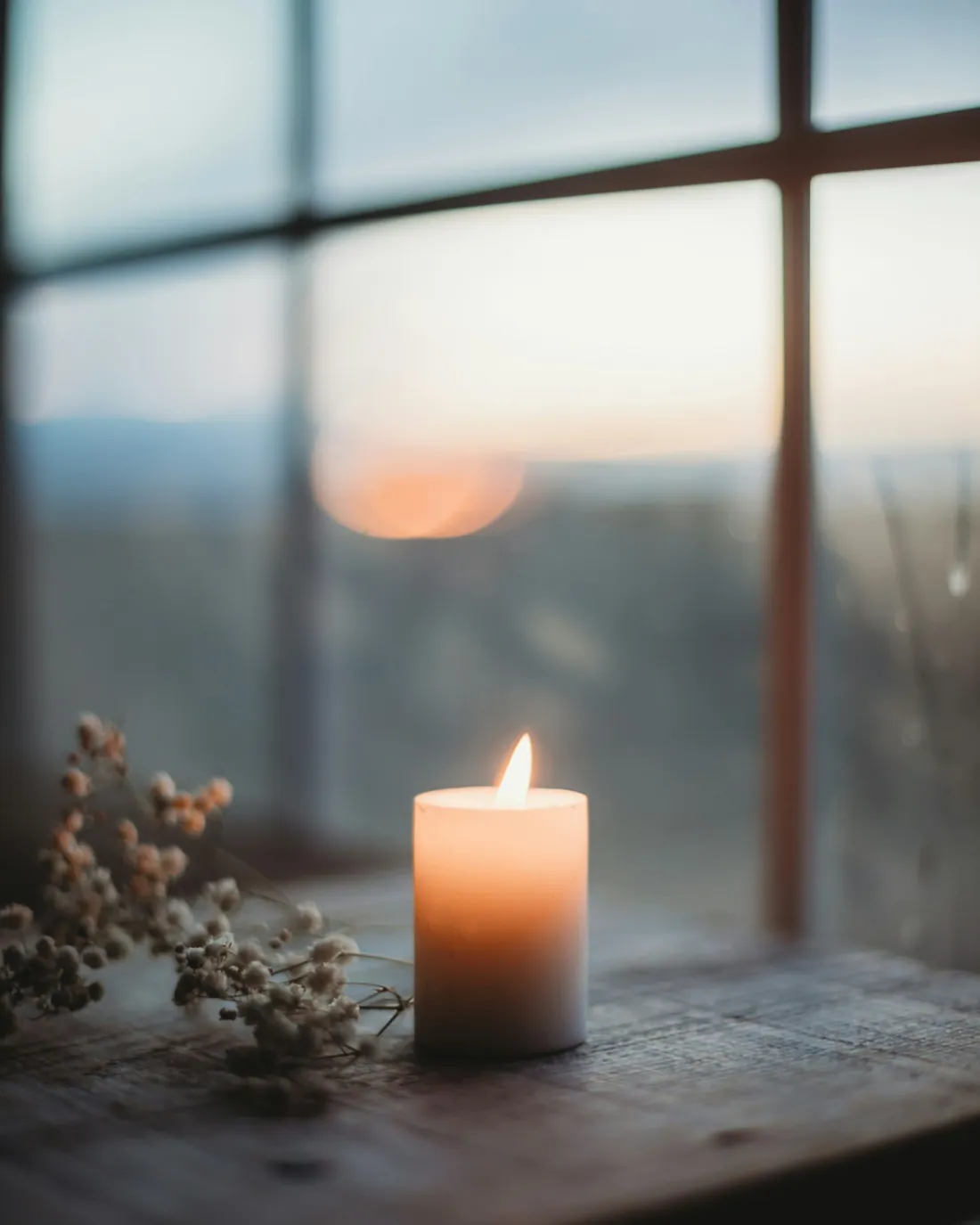 Single candle glowing on a windowsill at dusk