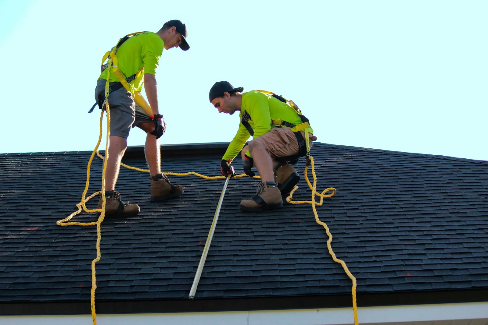 Two roofers in harnesses measuring a shingle roof