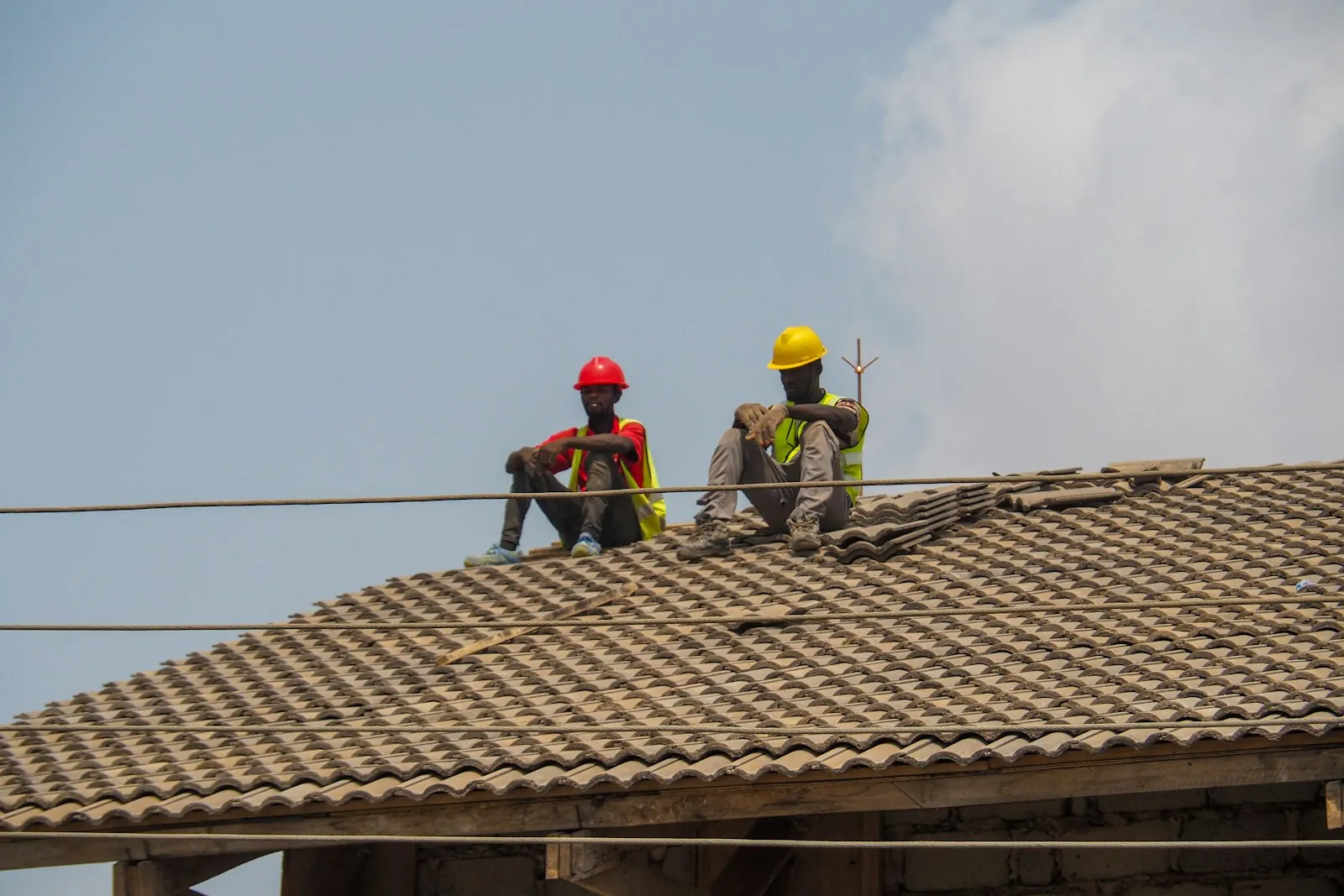 Two roofers in hard hats sitting on a tile roof