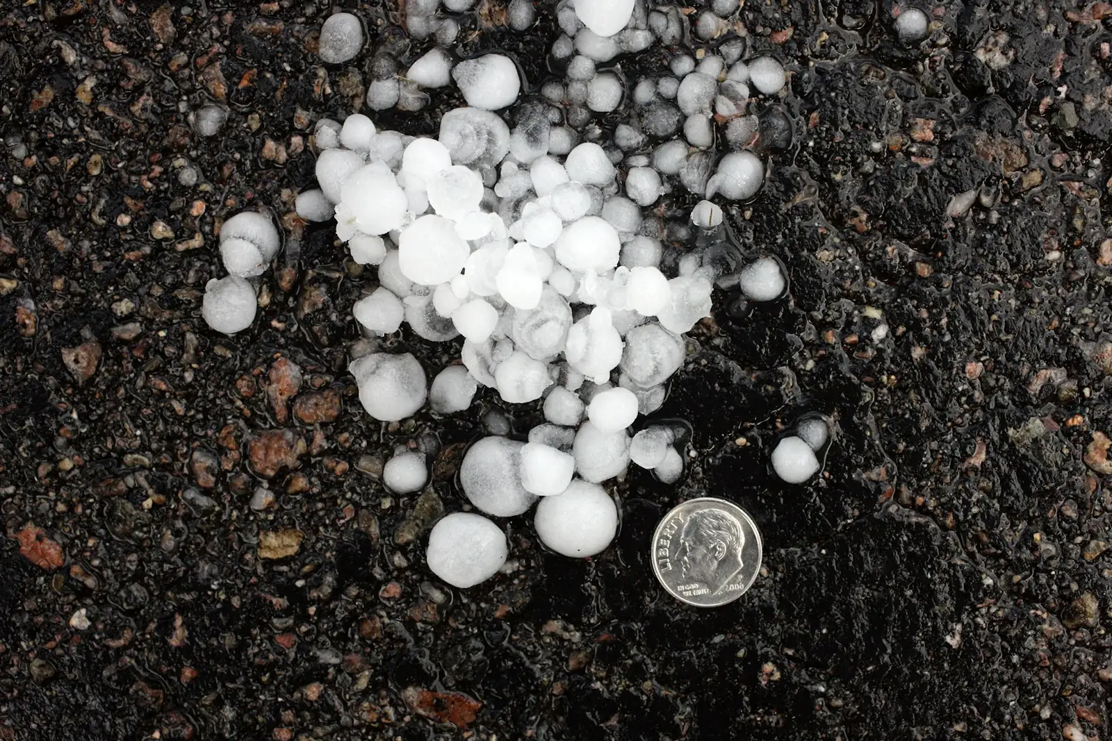 Hailstones on dark ground next to a coin for scale