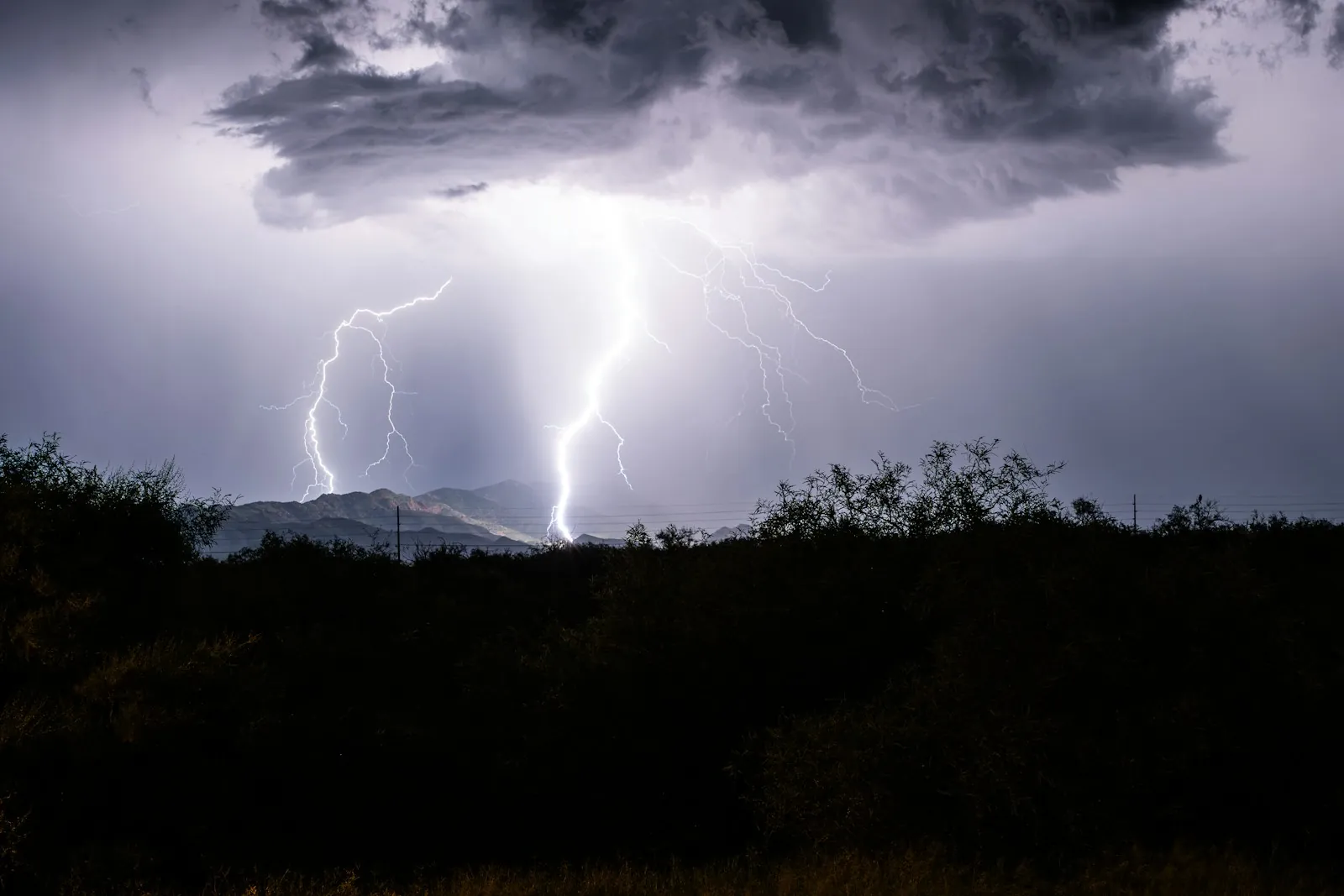 Lightning bolts striking behind a dark desert ridge under a purple monsoon sky
