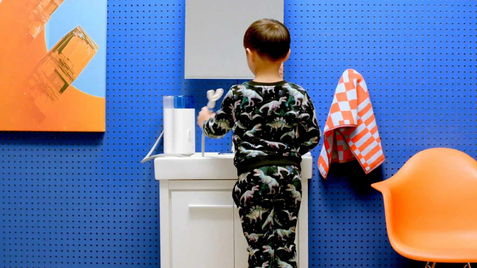 Young child brushing teeth at a small sink against a blue wall