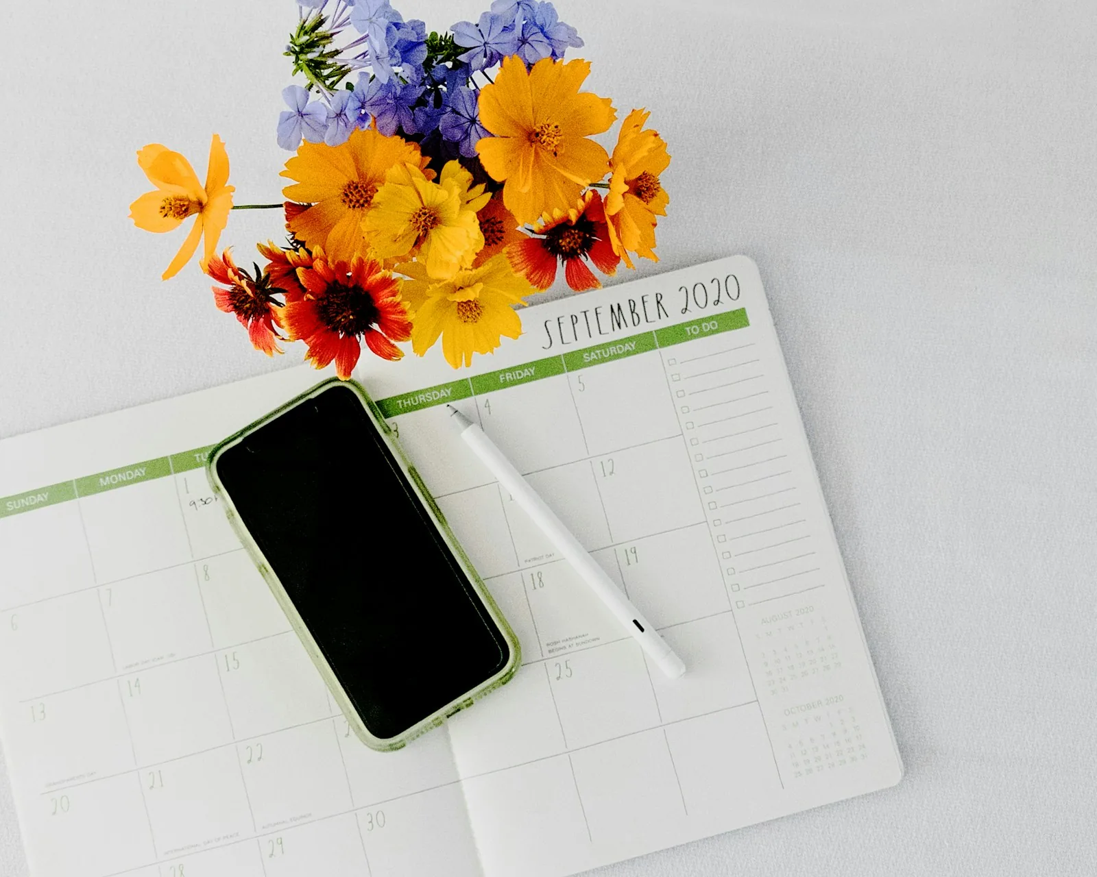Phone resting on a paper planner beside fresh flowers