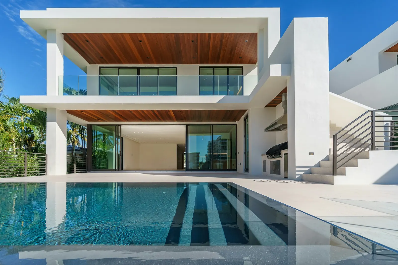 White two-story modern home with wood soffits above a long pool
