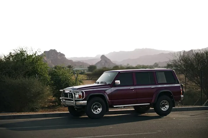 SUV parked on a desert road with red rock hills behind