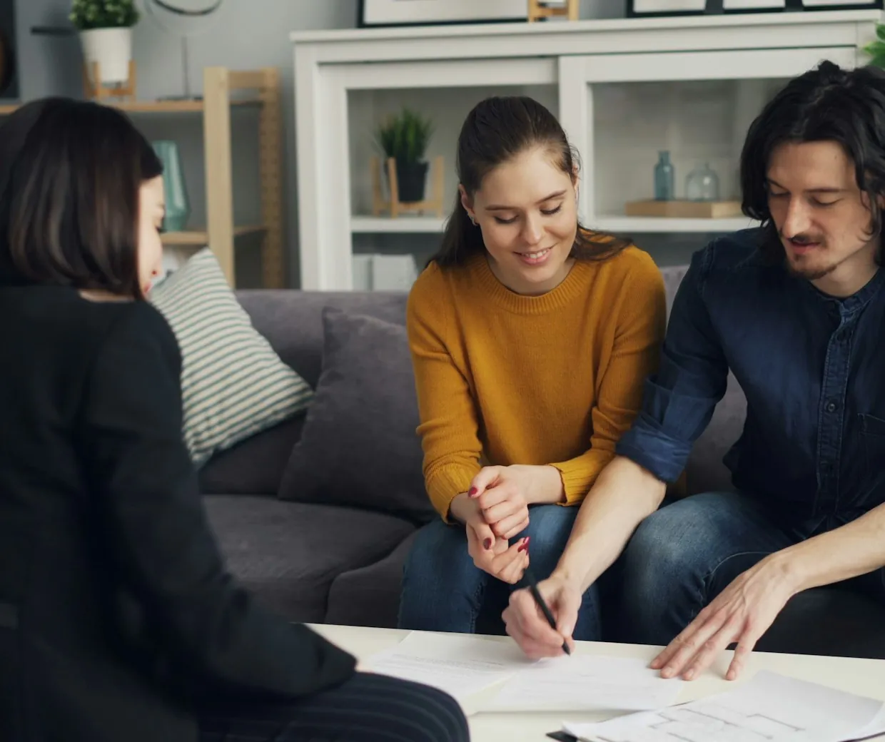 An advisor reviewing paperwork with a smiling couple on their living-room sofa