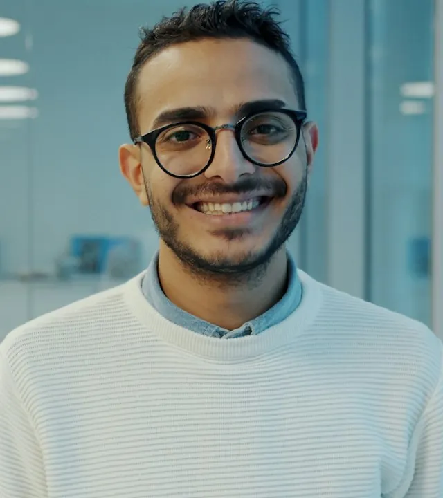 Portrait of Omar Haddad, a smiling agent with glasses and a light sweater