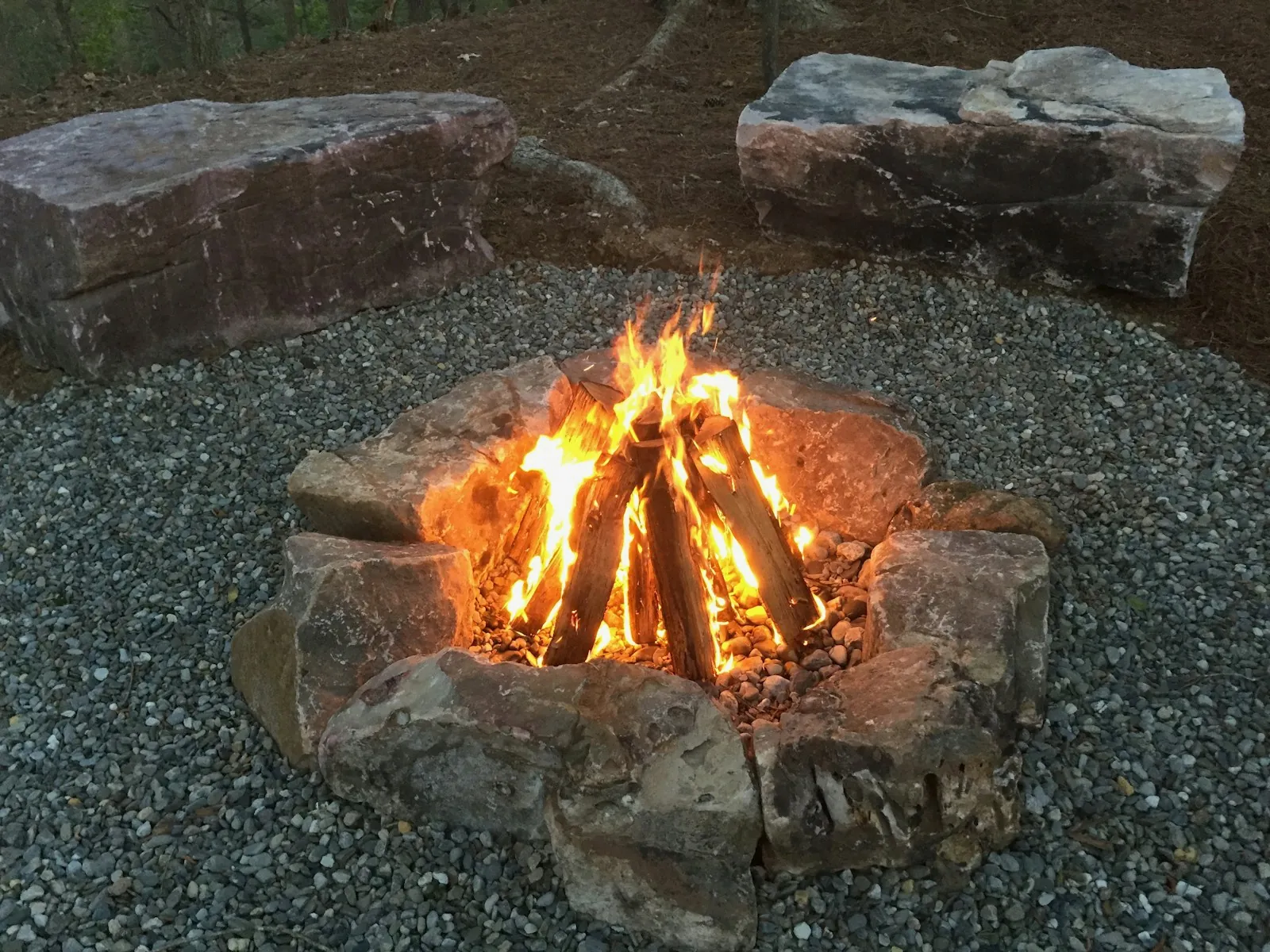 Stone fire pit burning in a gravel courtyard at night