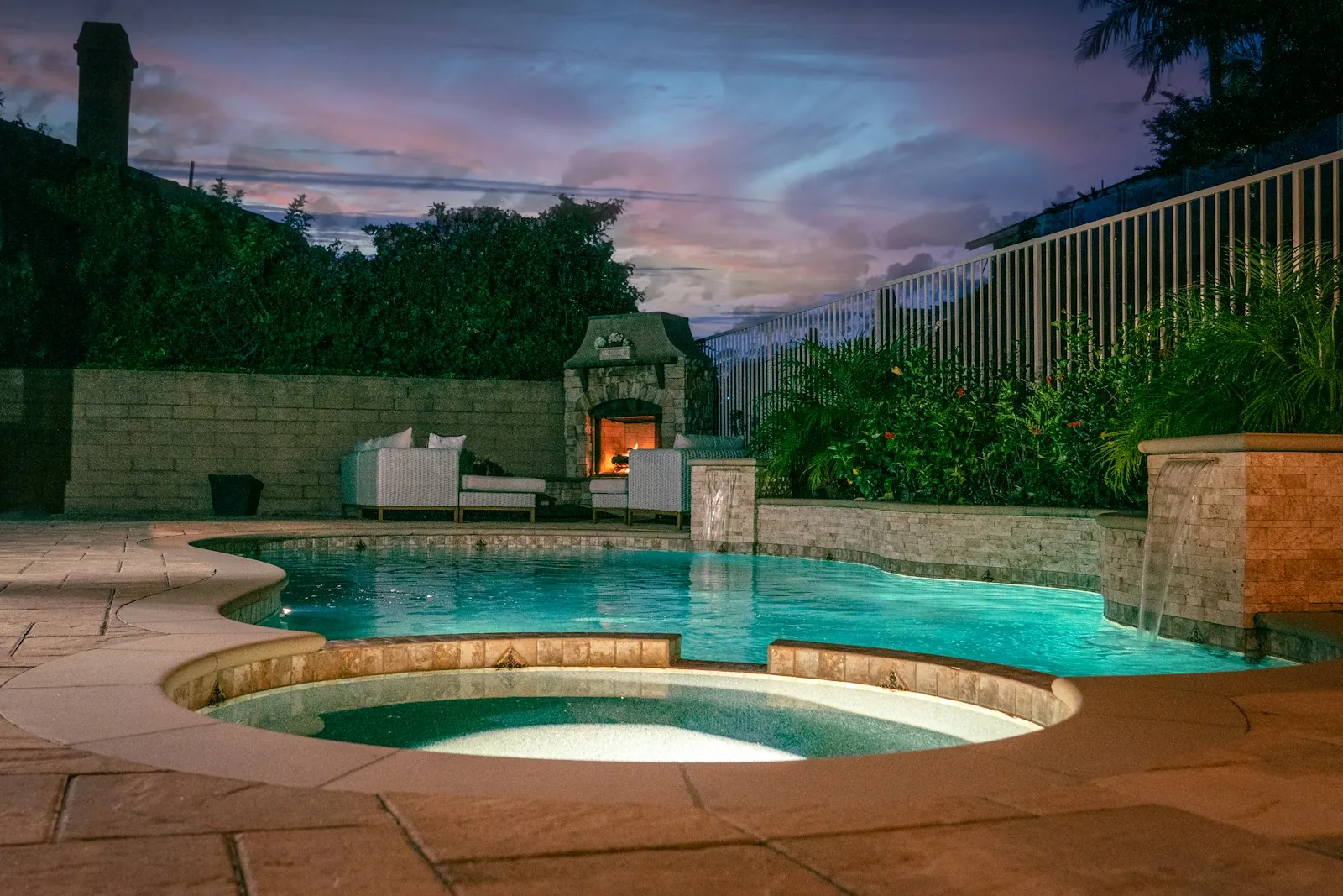 Backyard pool and spa with an outdoor fireplace at dusk