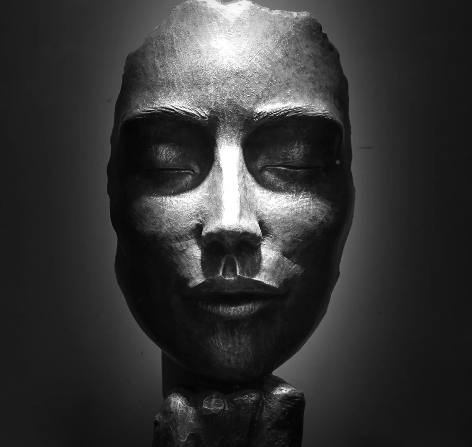 Silver sculpted face mask lit dramatically in the dark