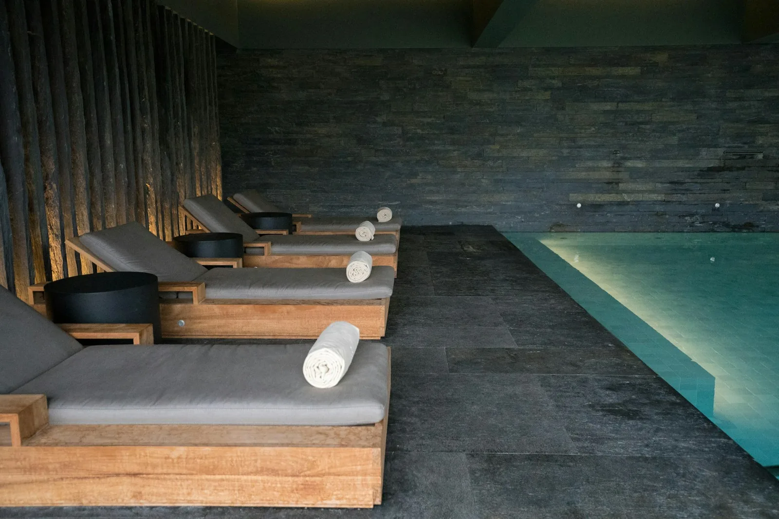 Low-lit spa pool with loungers and slate walls