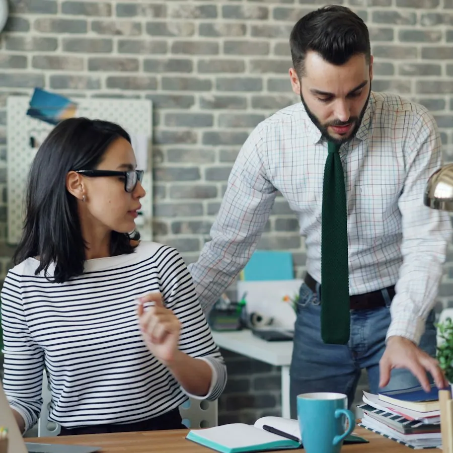 Technician in a tie helping a colleague at her laptop in a small office