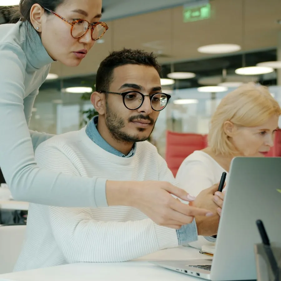 Colleague leaning over to help a coworker set up his laptop