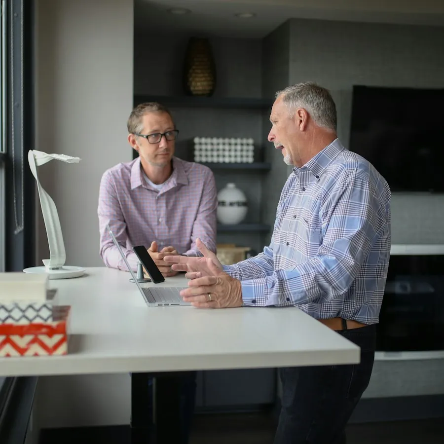 Two colleagues talking at a desk by the window of a small property management office