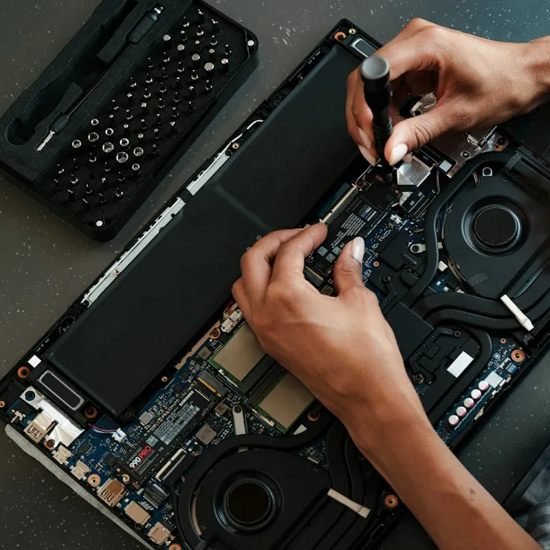 Hands installing a new drive in an opened laptop beside a screwdriver kit