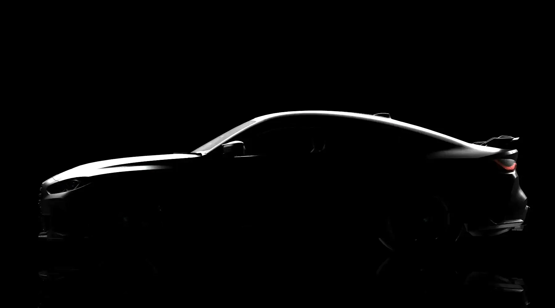 Black sports coupe in silhouette in a dark studio, its roofline traced by a single light