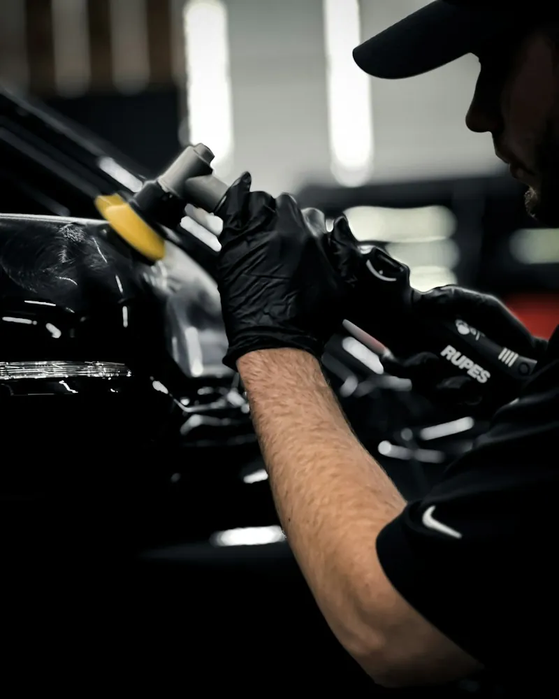 Gloved hands guiding a polisher across black paint (studio loop)