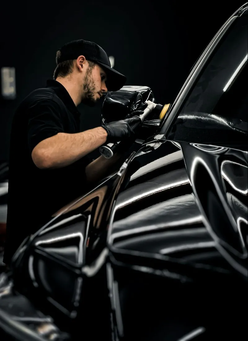 Detailer machine-polishing the glossy black flank of a car