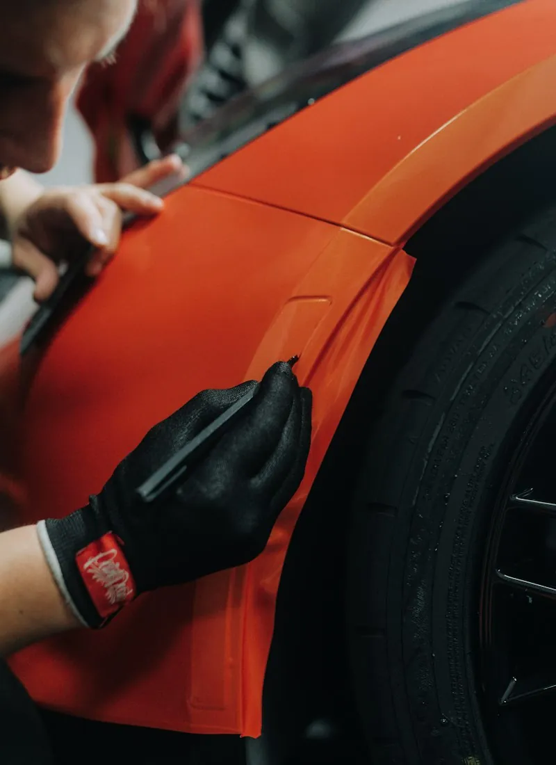 Gloved installer smoothing clear protection film along a fender edge