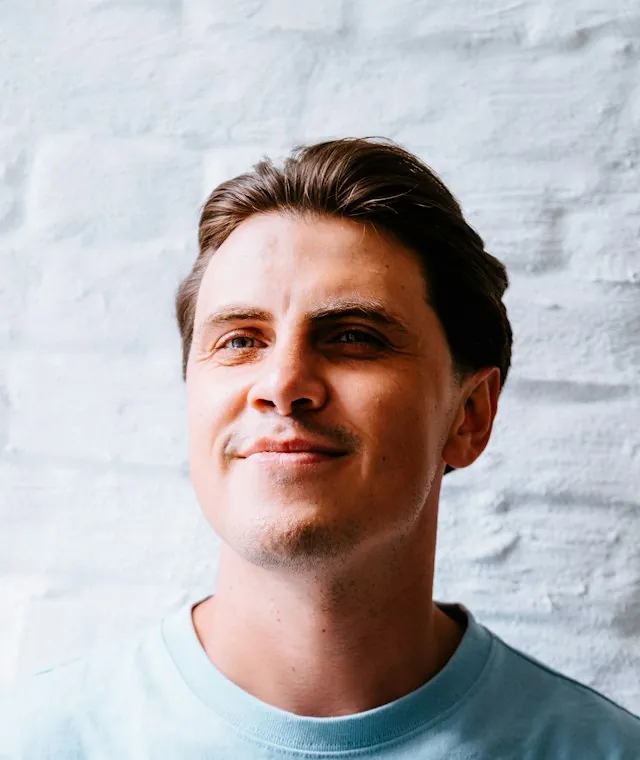Smiling man in a light blue T-shirt against a white brick wall