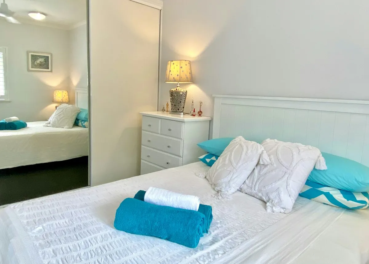 Neatly made white bed with teal pillows and rolled teal towels