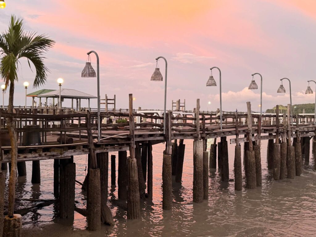 A long wooden pier with lamp posts at a pink sunset in Thailand, photographed by Adam Neuerburg